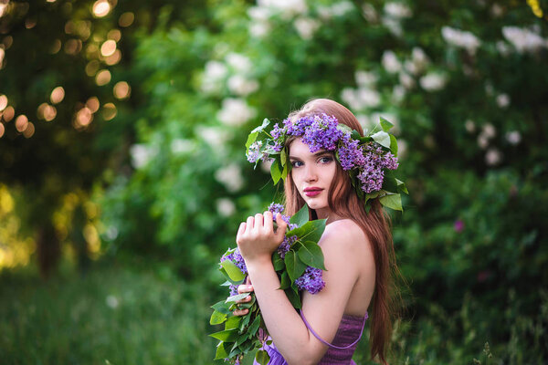The girl with the wreath on his head in the lilac bushes