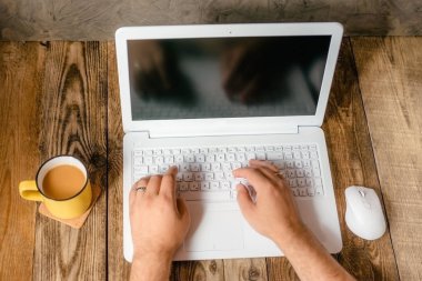 Erkekler ellerini beyaz dizüstü bilgisayar ve ahşap zemin üzerine sarı Kupası