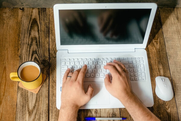 men hands with white laptop and a yellow Cup on wooden background