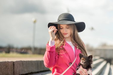 çekici kız siyah bir şapka ve pembe bir ceket ile alan gezinti yolu üzerinde bir köpek yürüyüş