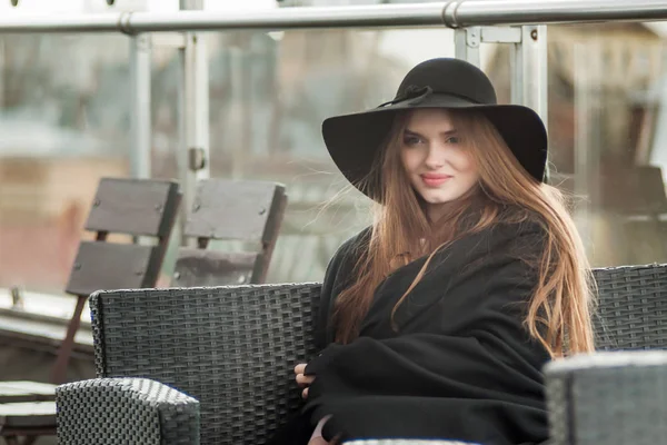 Kız bir siyah şapka çapında ekledi ve restoranın terasında oturup pelerin — Stok fotoğraf