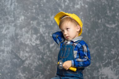 bir çocuk bir sarı inşaat kask içinde çizikler kafasını ve bir çekiç tutma