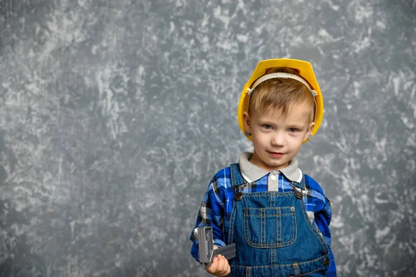 Um menino segura um capacete de construção e sorri — Fotografia de Stock