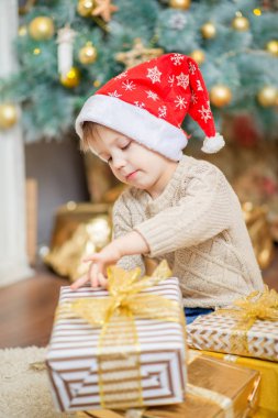 kırmızı bere içinde bir oğlan bir Noel ağacının yanında bir hediye ile oturuyor.