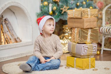 kırmızı bere içinde bir oğlan bir Noel ağacının yanında bir hediye ile oturuyor.