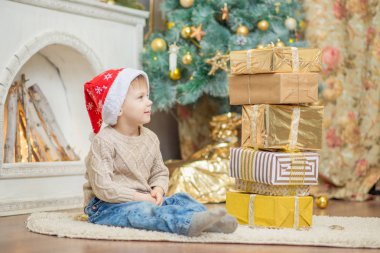 kırmızı bere içinde bir oğlan bir Noel ağacının yanında bir hediye ile oturuyor.