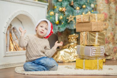 kırmızı bere içinde bir oğlan bir Noel ağacının yanında bir hediye ile oturuyor.