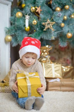 Kırmızı şapkalı bir çocuk bir Noel ağacı bir hediye ile oturuyor.