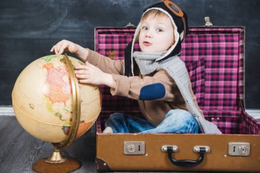 bir bavul küre içinde oturan çocuk pilot