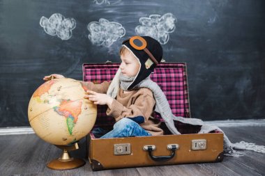 bir bavul küre içinde oturan çocuk pilot