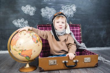 bir bavul küre içinde oturan çocuk pilot