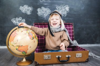 bir bavul küre içinde oturan çocuk pilot