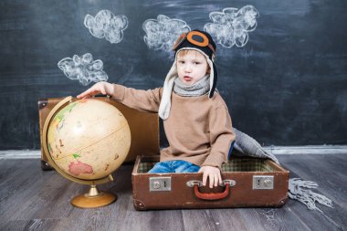 bir bavul küre içinde oturan çocuk pilot