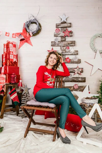 Ein Mädchen im roten Pullover mit einem Hirsch auf dem Hintergrund der Weihnachtsdekoration — Stockfoto