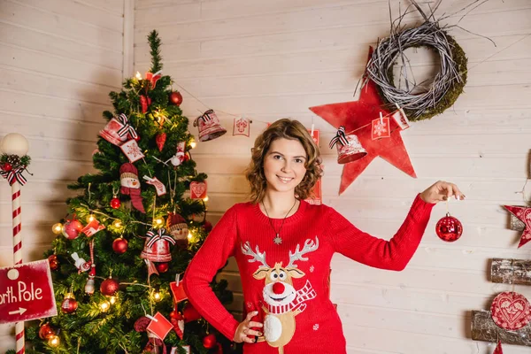 Ein Mädchen im Hirschpullover hält eine Weihnachtskugel in der Hand — Stockfoto