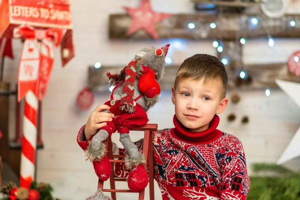 Chłopiec w czerwonym swetrze świątecznym z miękkim symbolem myszy zabawki roku — Zdjęcie stockowe