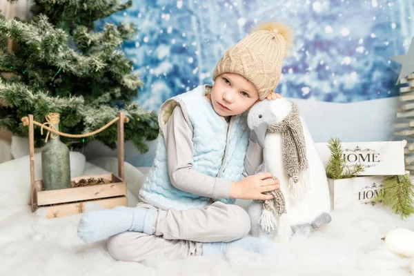 Año nuevo y Navidad. Niño sentado con pingüino de juguete suave sobre fondo decorado de invierno — Foto de Stock