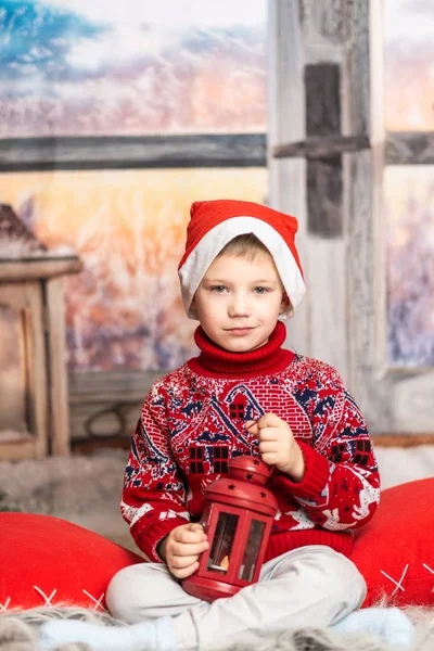 Mały chłopiec w świątecznym kapeluszu i czerwonym swetrze siedzi z latarnią — Zdjęcie stockowe