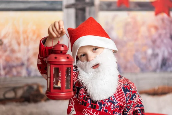 Małego chłopca przebranego za świątecznego gnoma z brodą trzymającego czerwoną latarnię — Zdjęcie stockowe
