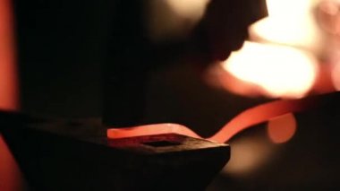 Smith çekiç üzerinde metal bir parça atıyor.