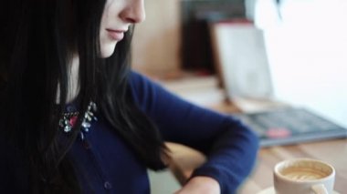 Güzel seksi esmer kapuçino içiyor ve fotoğraflar ile ilgilenen bir kafede oturup kağıda basılmış