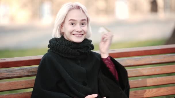 Frau in den Händen eines Smartphones und einer goldenen Kreditkarte sitzt auf einer Bank und zeigt glücklich eine Zahlungskarte — Stockvideo