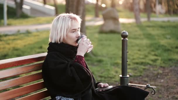 Blond žena dívka venku v rukou smartphone sedí na dřevěnou lavici nápoje cofee čekání