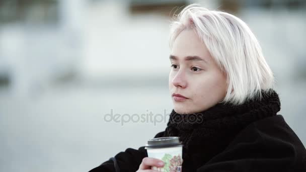 Blond dívka venku na pláži pije kávu, jak vypadá do dálky klidně usmívá detail — Stock video
