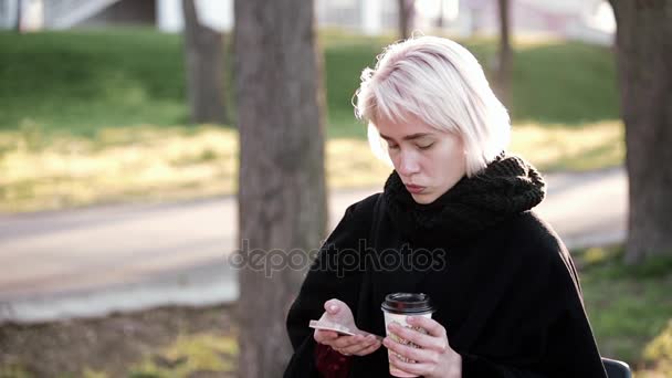 밖에 서 금발 소녀입니다. 스마트폰 및 마시는 커피의 손. 스마트폰에 텍스트 입력 — 비디오
