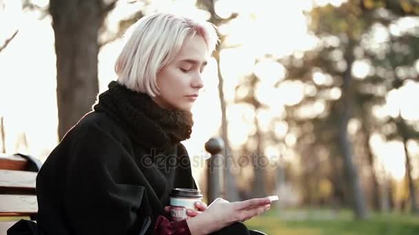 Chica rubia sostiene café mira el teléfono inteligente gira abruptamente cámara Sorpresa en la cara Llamada — Vídeo de stock