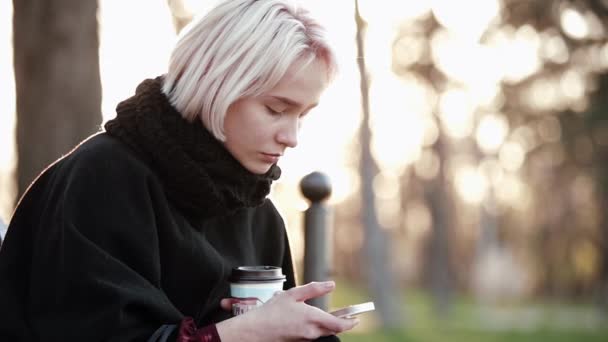 Menina loira lá fora Nas mãos de um smartphone e café Lendo infelizmente a mensagem no smartphone — Vídeo de Stock