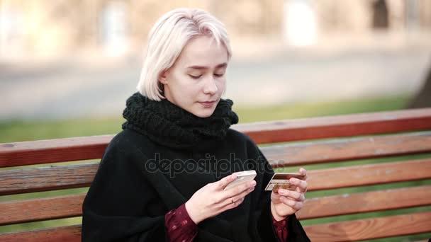 Щаслива дівчина блондинка зовні виконує транзакцію цю золоту платіжну кредитну картку на смартфон — стокове відео