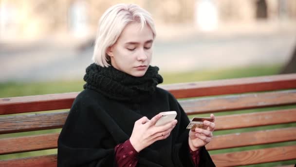 Sorgliga blond flicka utanför utför transaktioner guld betalning betalkort kreditkort till din smartphone — Stockvideo