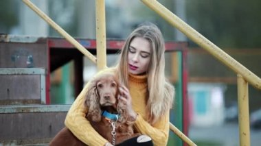 Sarışın kadın ve köpek yavru horoz İspanyol vuruş şehirde akşam köpek umurunda öpücük gülümsüyor