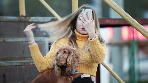 Blondynka i pies cocker spaniel dostosowuje jej włosy patrząc na odbicie na smartfonie Internet — Wideo stockowe