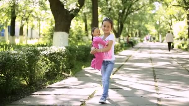 Маленькая девочка брюнетка латынь, гуляющая в парке со своей игрушечной куклой — стоковое видео
