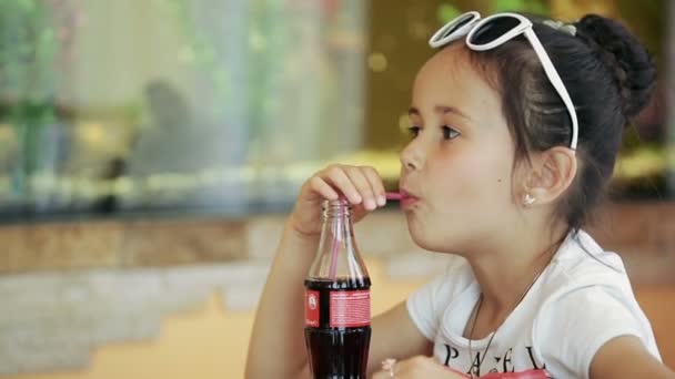 Liten flicka brunett latina sitter i café dricker läsk cola mot bakgrund av ett akvarium — Stockvideo