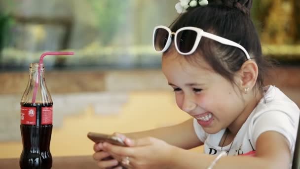 Meisje kind brunette latina zitten in Cafe, spelen op smartphone in het spel glimlachend in verlegenheid gebracht — Stockvideo