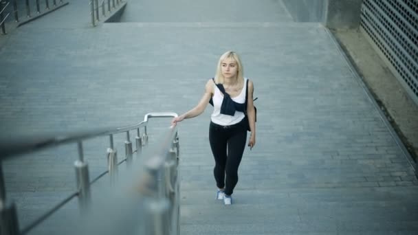 Unga blonda kvinnan klättrar i trappan i staden. Rör sig mot kameran och passerar. — Stockvideo