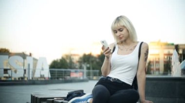 Sarışın genç kadın bir tezgah kullanır smartphone parlamaya günbatımı ışık camdan yansıyan oturur