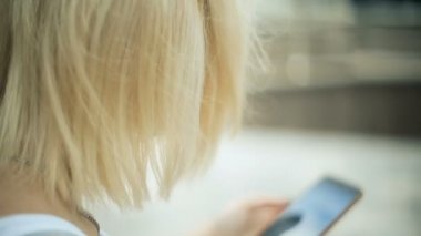 Parkta, sarışın genç kadın bir akıllı telefon, internet, metin kullanır, sessizce arka görünümünde gezinirseniz görünüyor