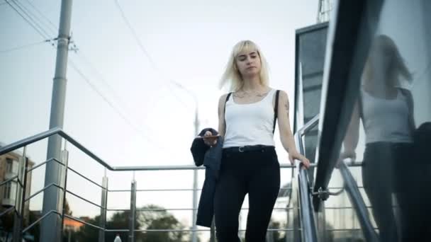 Молода блондинка йде по сходах міста. Рухається в бік камери . — стокове відео