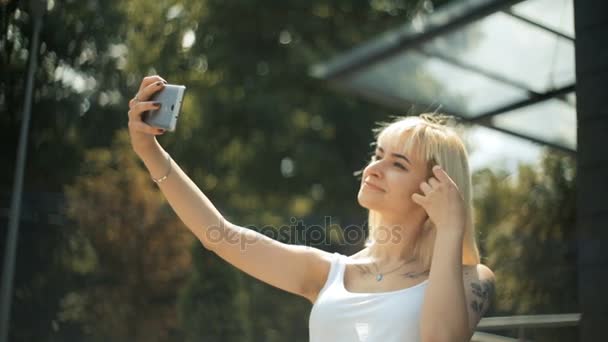 Joven rubia haciendo una foto selfie, sonriendo, expresa una emoción diferente — Vídeos de Stock