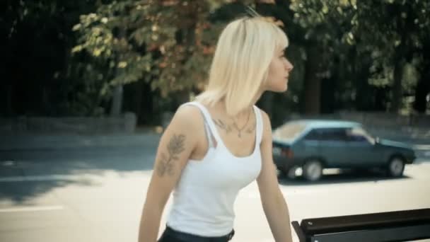 Mujer rubia joven camina en la ciudad se sienta en el banco lee el mensaje en el teléfono inteligente en silencio — Vídeos de Stock