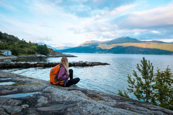 Jeune femme avec sac à dos debout sur la côte du fjord — Photo