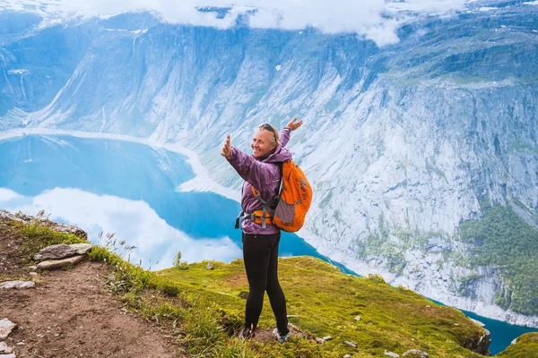 Ung kvinde med rygsæk stående på fjordkysten - Stock-foto