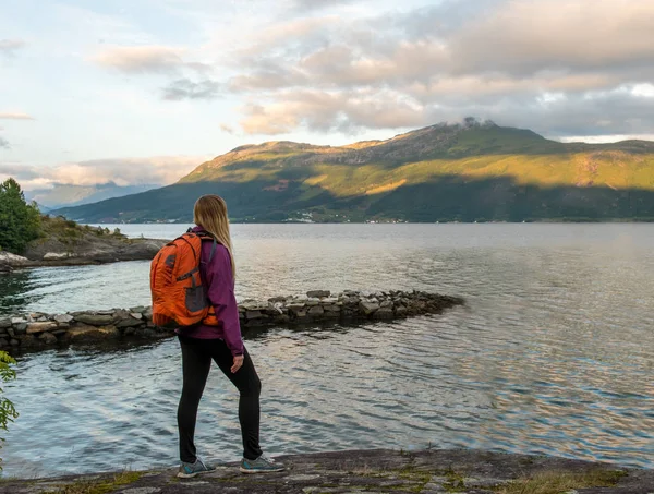 Mladá žena s batoh stojí na pobřeží fjordu — Stock fotografie