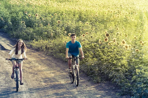 Teen couple riding bike in sunflower field — Stock Photo, Image