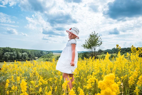 Cute little laughing girl walking in field of yellow flowers — Stock Photo, Image