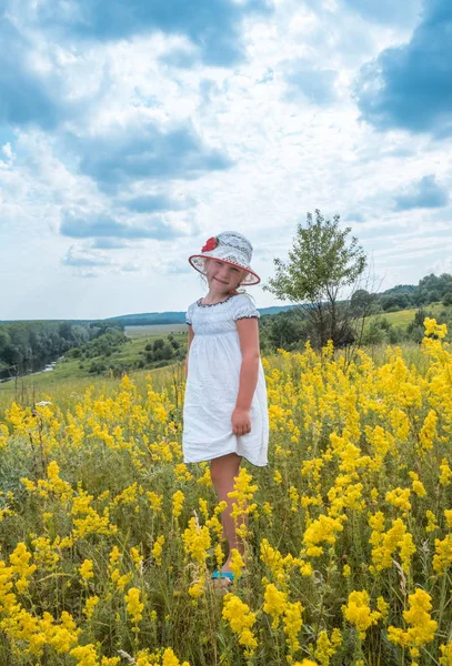 Niedliche kleine lachende Mädchen zu Fuß in Feld von gelben Blumen — Stockfoto